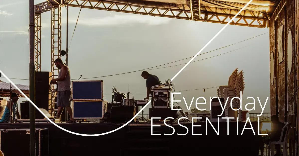 Event crew setting up equipment on an outdoor stage with the words “Everyday Essential.”